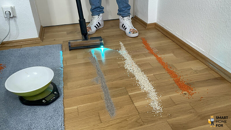 Saugtest der Dreame Z40 Station auf Hartboden mit Sand, Haferflocken und Linsen – gut sichtbar mit aktiver Blaulichtausleuchtung.
